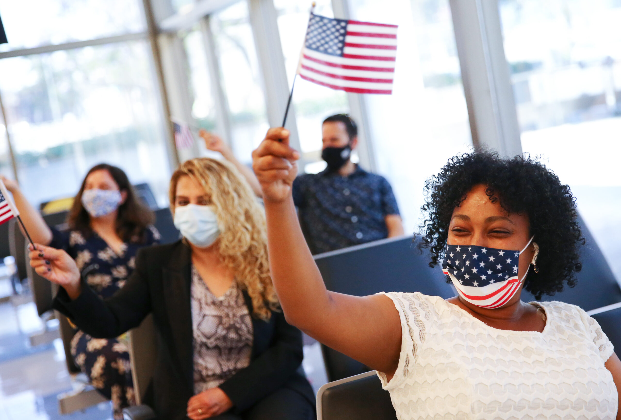 LOS ANGELES, CALIFORNIA - JUNE 17:  New U.S. citizens including Selamawit Berhane (R), originally from Ethiopia, wave American flags during a special World Refugee Day naturalization ceremony on June 17, 2021 in Los Angeles, California. 26 new U.S. citizens, most of whom are refugees, were sworn in at the U.S. Citizenship and Immigration Services (USCIS) ceremony. (Photo by Mario Tama/Getty Images)